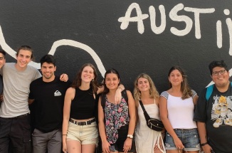 Group of students smiling in front of black mural with white outline of Texas