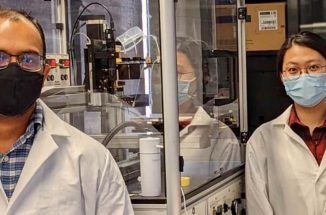 Four researchers stand in a lab in front of a glass box holding technological equipment