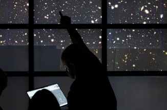People stand silhouetted in front of a screen display filled with stars from the night sky