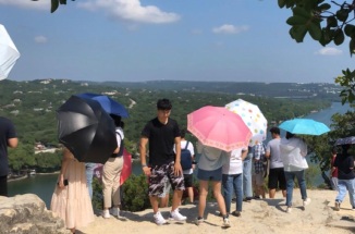 International students hold umbrellas, looking out over Mt. Bonnell in Austin