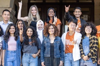 College students of many races smile and throw the UTexas 'Hook 'em Horns" symbol
