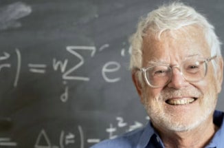 UT physicist Allan McDonald smiles by a blackboard bearing equations