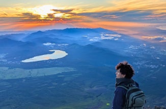 UT student stands in front of a blue mountain and orange sunrise