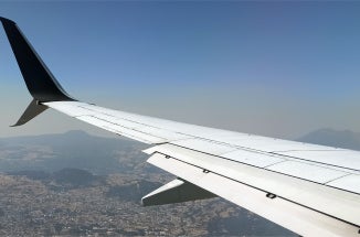 An airplane wing over an aerial landscape of a mountainous city