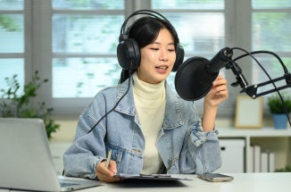 A woman with headphones speaks into a podcasting microphone.