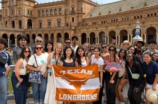 Students hold up a "Texas Longhorns" Flag in front of a Castle.