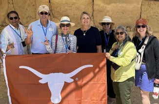 A group of travelers hold a "Longhorns" flag in front of ruins.