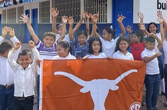 Children in Nicaragua hold up a "Texas Longhorns" flag in front of a school.