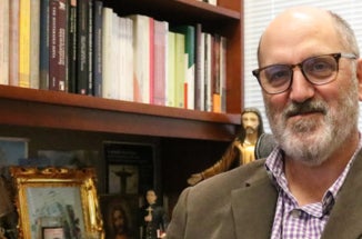 A professor poses for a portrait in his office, in front of a bookshelf.