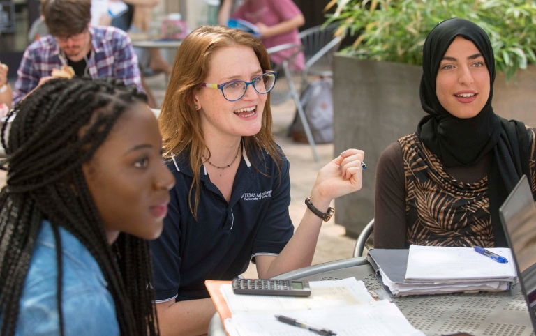Female students interact together at an outdoor table on campus