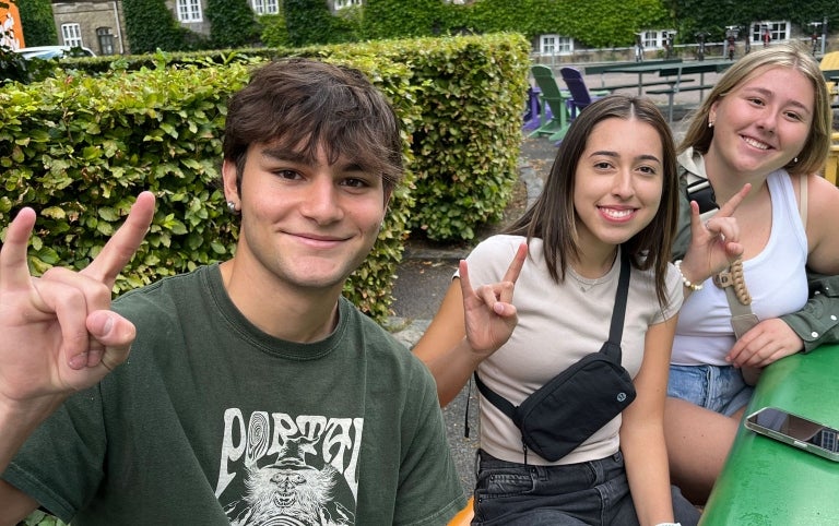 Three students displaying the hook'em sign smile for a photo abroad in Denmark
