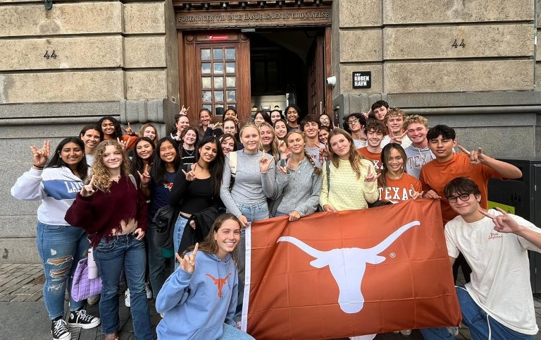 A study abroad group smiles for a group photo holding the UT Flag in Denmark