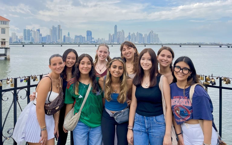 A group of female study abroad students smile as they pose for a photo with the ocean and Panama city skyline in the background