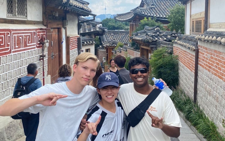 A group of male students smile and show the Longhorn hook'em sign while exploring and iconic area of South Korea
