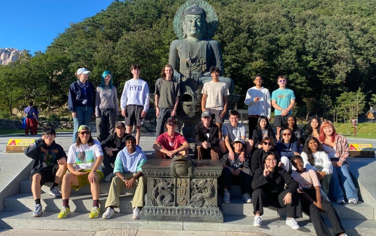 A study abroad group poses in front of a statue of Buda with mountains in the background in South Korea