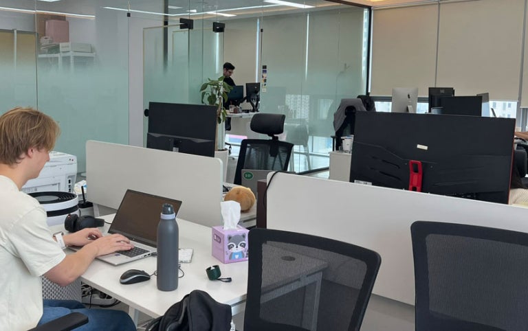A male participant with Absolute Internships works in an open concept office setting at Packative