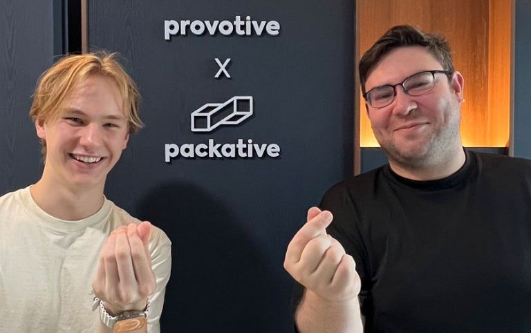 Two male participants with Absolute Internships smile in front of the Packative office sign