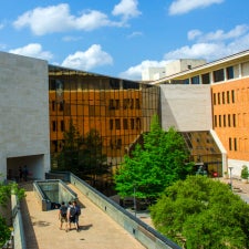 The facade of the UT Austin McCombs School of Business on a blue sky and puffy cloud day
