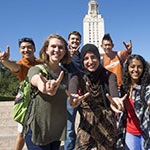 diverse students doing hook'em sign with UT tower in the background.