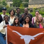 Students smile in a group photo taken in England while holding a UT longhorn flag