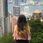 A student looks out from a high vantage point on a cloudy day at the city skyline of Hong Kong and the bay that surrounds it