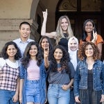 Smiling ISSS students pose for a group photo on the main building stairs while displaying the hook'em sign
