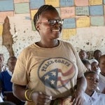 A smiling female peace corps volunteer aids with teaching in an African school