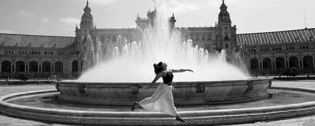 A woman gracefully leaps in front of a fountain in Seville, Spain.