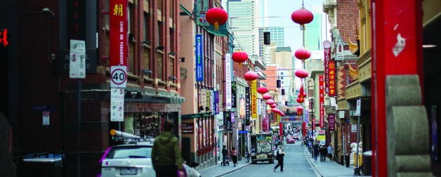 street with shops lined with hanging round red paper lanterns with people walking below