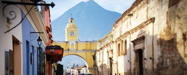 colourful buildings line street with yellow clock tower arch near mountain during daytime