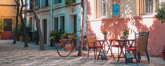 outdoor chairs and tables near colourful buildings and bicycle in shade during daytime