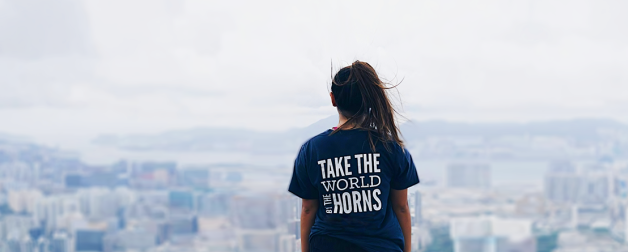 image of female looking out on city landscape with blue T-shirt reading "Take the World by the Horns"