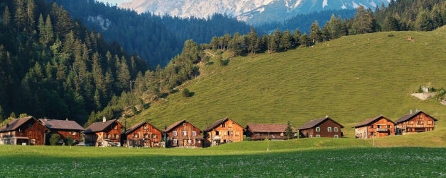 row of brown houses in green hills near trees and snowy mountains during daytime
