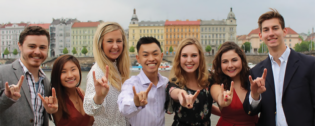 seven students doing the hook 'em sign in front of scenery
