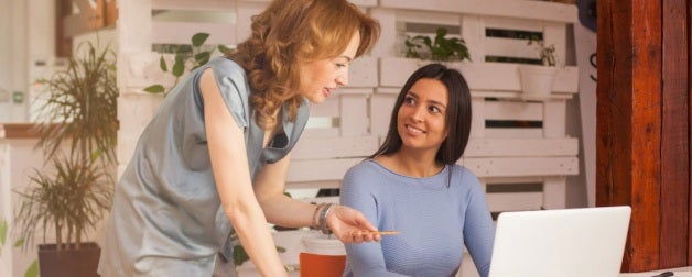 A female advisor helps a smiling female student on a computer