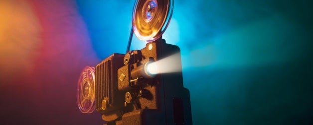 Film projector casting a movie onto a screen in front of a blue, pink, and gold background