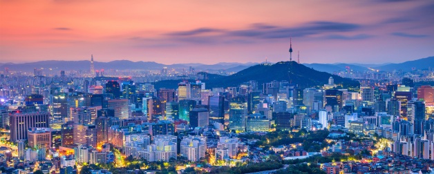 Cityscape image of colorfully lit Seoul downtown with the mountains in the background during and orange and purple summer sunrise.