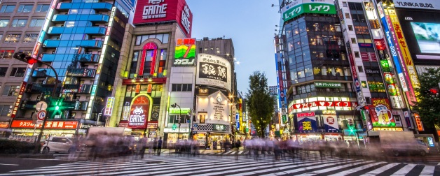 Street view of Shinjuku, Japan, illuminated with brightly colored lights and signs at night and busy with acitivity.