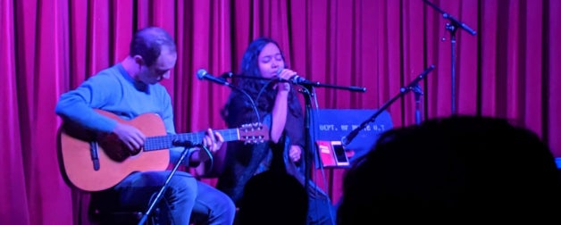 Two students performing on stage, one playing an acoustic guitar and one singing into a microphone