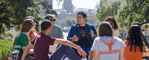 Students engaging in friendly discussion on the UT campus southlawn with Texas State Capitol in the background 