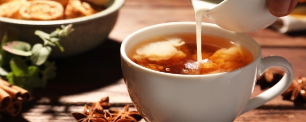 Herbs and pastries are displayed on a table as warm milk is poured into star anise tea.