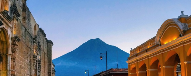 An old stone street and historic buildings in the foreground frame the distant Agua volcano in Antigua Guatemala in the evening during the blue hour