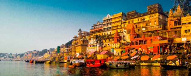 Colorful yellow, orange, and white buildings sit on the right side of a river with self-made boats in Asia