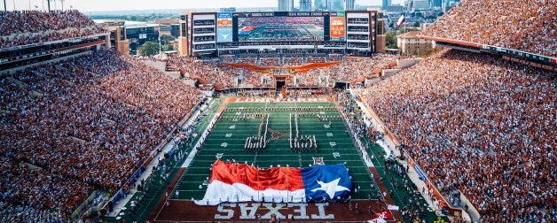 A view from the UT Austin Football stadium as seen from a spectators point of view in packed stadium with scoreboard and Austin city skyline in the background