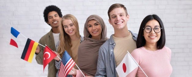 A diverse group of exchange students smiling and holding flags representing different countries