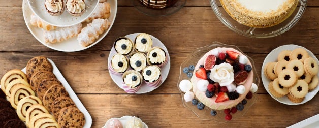Wooden table with cake, pies, cupcakes, tarts and cake pops.