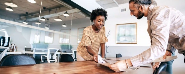 Two people have a talking in an office and going over a piece of paper