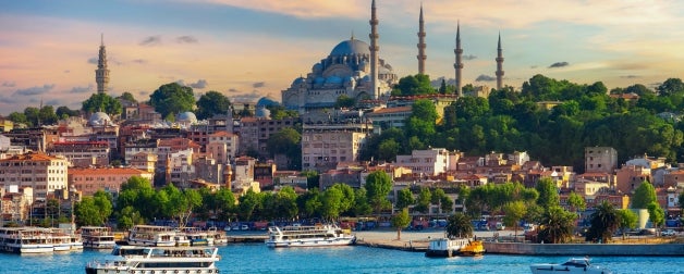 Tourist sightseeing ships cruise the aquarmarine waters that touch the city of Istanbul, Turkey with the impressive Suleymaniye Mosque in the background