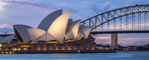The illuminated Sydney Opera House and Harbor Bridge backdropped by an evening blue and pink sunset in Sydney, Australia