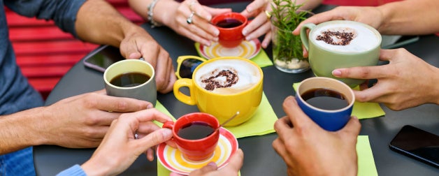 people sitting at a round black table holding cups of coffee and cappuccino while spending time together